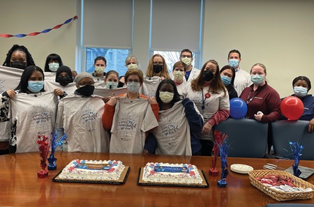 A group of employees gather with T-shirts and cake that both celebrate the launch of the Penn Center for Living Donation 